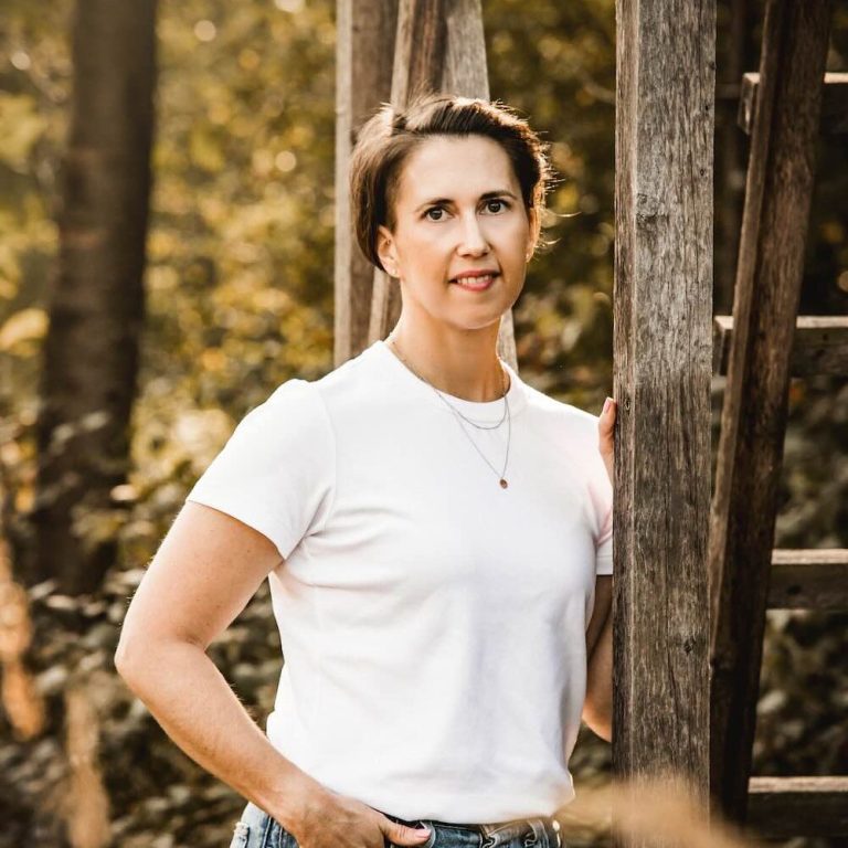 Porträt von Linda Hanzlik, Coachin für ganzheitliche Gesundheit, angelehnt an einen Hochsitz im Wald.