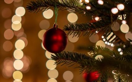 Nahaufnahme eines Tannenzweigs mit einer roten Christbaumkugel vor verschwommenen Lichtern – Symbol für einen achtsamen Advent und Ruhe.