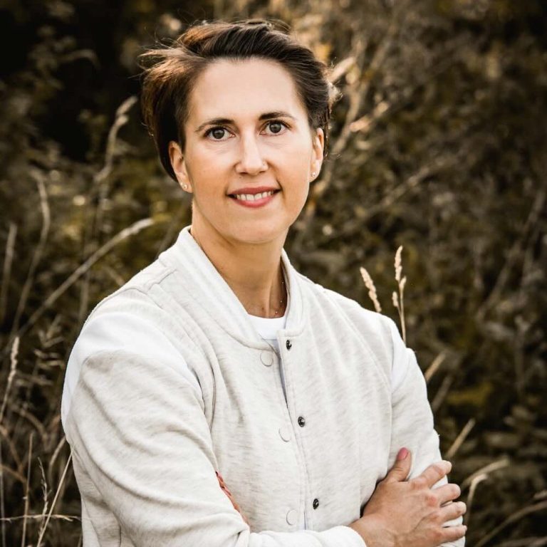 Porträt von Linda Hanzlik, mit verschränkten Armen auf einer Wiese – Expertin für Gesundheitsprävention und Coachin für Unternehmen.