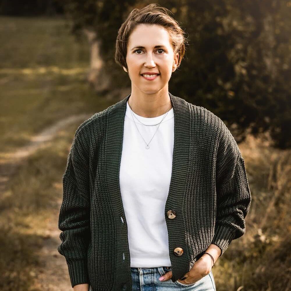 Porträt von Linda Hanzlik, Coachin für ganzheitliche Gesundheit, lächelnd auf einem Feldweg in der Natur.